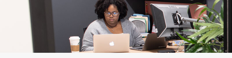 A student worker works at her laptop in an office.